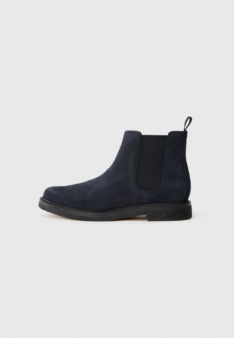 Bottines Chelsea en daim bleu marine avec un panneau élastique latéral noir, une languette au talon et une semelle en caoutchouc noire sur un fond blanc.