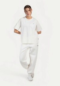 Witte katoenen T-shirt met een losse pasvorm, ronde hals en korte mouwen. Gecombineerd met witte joggingbroeken met zijzakken en logo-accenten.