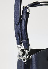 Gros plan sur une sangle de sac à main en cuir texturé bleu foncé avec des fermoirs métalliques argentés et une boucle réglable.