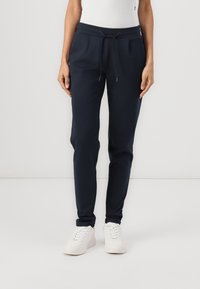 Marinblå joggerbyxor i bomullsblandat tyg, med elastisk midja, justerbar dragsko och sidofickor, kombinerade med vita sneakers.