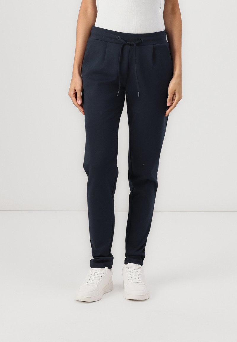 Marinblå joggerbyxor i bomullsblandat tyg, med elastisk midja, justerbar dragsko och sidofickor, kombinerade med vita sneakers.