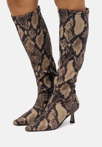 Bottes hautes en cuir imprimé serpent beige et marron, avec un design texturé et décontracté, un bout pointu et un petit talon.