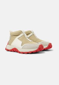 Chaussures montantes en tissu beige avec des accents blancs et gris, semelle en caoutchouc rouge, et fermeture éclair, texturées pour l'adhérence et la durabilité.