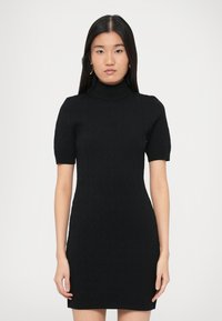 Crna pletena haljina s visokim ovratnikom, kratkim rukavima i pripijenim krojem. Ima teksturirani uzorak na cijelom tkanju.