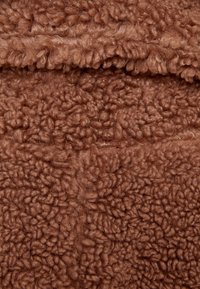 Brun, texturerad tyg med en fluffig, fleece-liknande yta. Ytan är mjuk med ett uttalat, vågigt mönster.