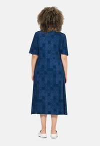 Blauwe, kort mouwige jurk met geometrische patronen, tot de knie, gemaakt van gladde stof. Heeft een losse pasvorm en uitsneden aan de zijkanten.