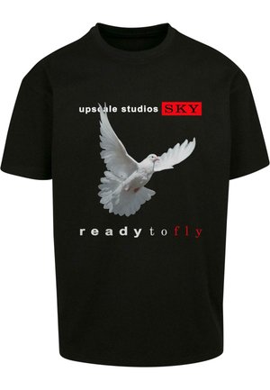 Juodas trumpas rankovės T-shirt su grafika, vaizduojančia baltą balandį skrydžio metu. Tekstas apima "upscale studios SKY" ir "ready to fly" raudona ir balta spalvomis.