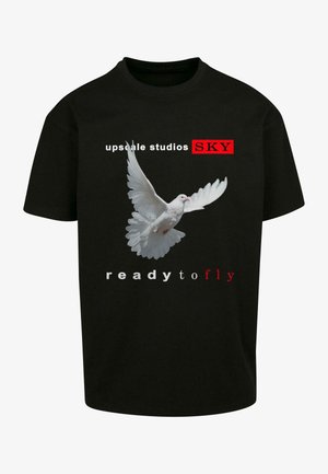 Czarny T-shirt z krótkim rękawem z grafiką białego gołębia w locie. Na koszulce znajdują się napisy "upscale studios SKY" oraz "ready to fly" w kolorze czerwonym i białym.
