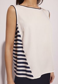Bez rękawów top w kremowe i granatowe paski, z gładką fakturą, okrągłym dekoltem i diagonalnym wzorem pasków po bokach.