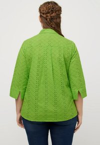Camicia in cotone verde con maniche 3/4, motivo a occhio di diamante, dettaglio con piega sul retro e spacchi laterali. Design semplice, texture leggera.