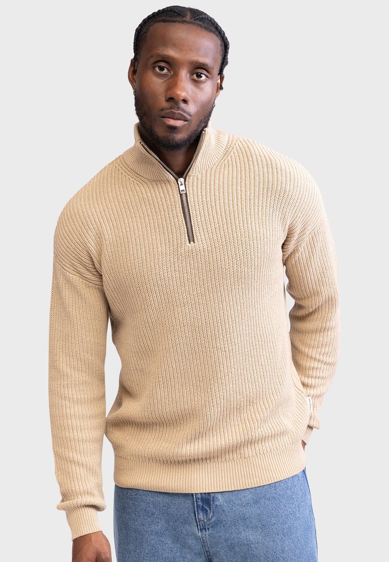 Beige genser med ribbestruktur, høy hals og glidelås halvveis. Lange ermer med noe løs passform. Enkelt design.
