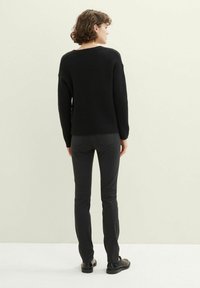 Juoda megzta džemperis su laisvu siluetu, apvalia iškirpte ir ilgomis rankovėmis, derintas su siaurais juodais kelnais ir juodais batais, matomas iš nugaros.