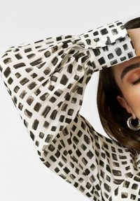 Button-up blouse featuring a white fabric with a black abstract print. The sleeves are gathered, creating a voluminous look with a smooth texture.