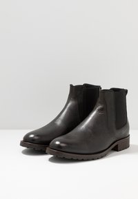 Bottes Chelsea en cuir noir à finition lisse, avec des panneaux élastiques sur les côtés, un embout arrondi et un petit talon empilé. Semelle texturée pour une meilleure adhérence.