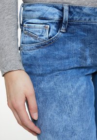 Modré denimové džíny s klasickým rovný fit, s designem pěti kapes, viditelnými detaily šití a jemným vyblednutím na látce.