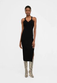 Črna oprijeta obleka s čipkastim robom, dolžine do kolen, z bočnim razporkom in tankimi naramnicami. Kombinirana s sijočimi škornji do kolen s kačjim vzorcem.