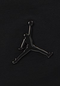 Țesătură neagră cu un logo Jumpman reflectorizant, care prezintă silueta unei persoane sărind cu o minge de baschet, textură netedă.