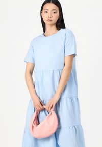 Vestido em camadas azul claro em tecido suave com mangas curtas. Modelo segura uma bolsa rosa arredondada com textura lisa.