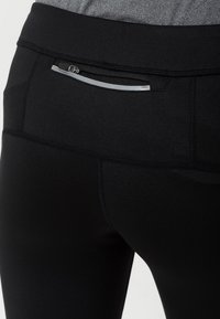 Czarne sportowe legginsy z zamkiem błyskawicznym w tylnej kieszeni z srebrnym akcentem, wykonane z gładkiego, elastycznego materiału.