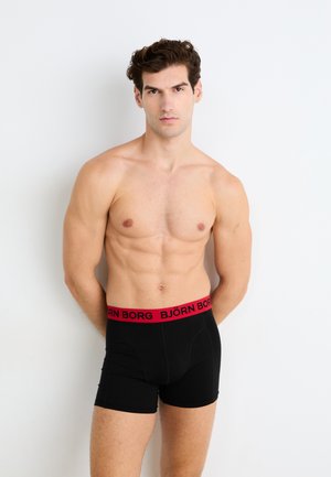 Schwarze Boxer Shorts mit einem breiten roten Bund, der mit "BJÖRN BORG"-Branding versehen ist. Der Stoff ist glatt und eng anliegend, entwickelt für Komfort und Unterstützung.