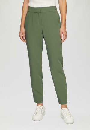 Grüne Slim-Fit-Hosen mit glatter Textur, Bundfalten und hohem Taillenbund, kombiniert mit weißen Sneakers für einen lässigen Look.