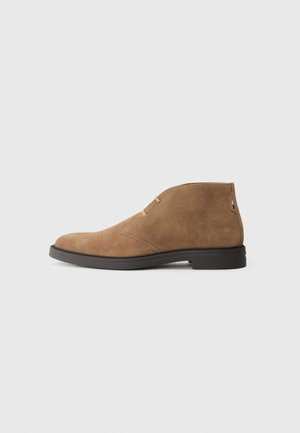 Bottes chelsea en suede marron avec un bout rond, un minimum de coutures et un petit talon en caoutchouc noir. Design classique, polyvalent pour diverses tenues.