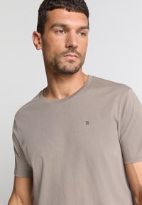 T-shirt met korte mouwen en ronde hals in licht taupe, met een klein zwart lijnontwerp op de borst, gemaakt van gladde, zachte stof.