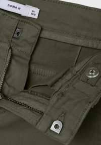 Olivgrüne Hose mit Reißverschluss, Druckknopf und genähten Taschen. Der Stoff hat eine glatte Textur mit einer strapazierfähigen Oberfläche. Etikett innen sichtbar.