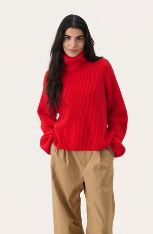 Rode geribbelde turtleneck trui met lange mouwen, gecombineerd met beige losse broek. De stof ziet er zacht en gestructureerd uit.