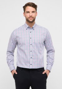 Witte blouse met lange mouwen en een roodblauw geruit patroon, voorzien van een button-down kraag en donkere knopen, gecombineerd met een zwarte broek.