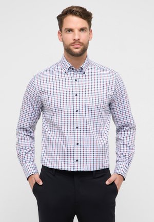 Witte blouse met lange mouwen en een roodblauw geruit patroon, voorzien van een button-down kraag en donkere knopen, gecombineerd met een zwarte broek.