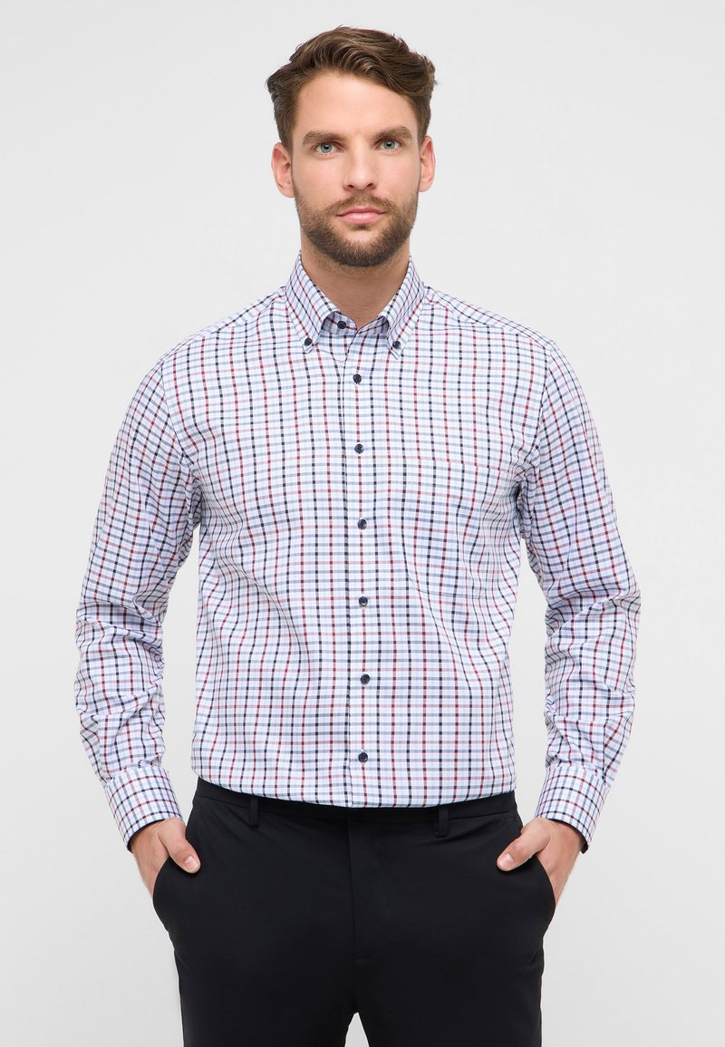 Witte blouse met lange mouwen en een roodblauw geruit patroon, voorzien van een button-down kraag en donkere knopen, gecombineerd met een zwarte broek.