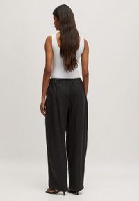 Zwarte, wijde broek met een verstelbare elastische tailleband, gemaakt van lichte stof. Gepaard met een aangesloten witte tanktop.