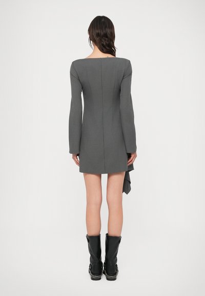 Szürke miniruha hosszú ujjakkal és négyzet alakú kivágással; hátul redőzött részlet díszíti, fekete középhosszú csizmával párosítva.