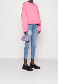 Różowy krótki sweatshirt, przetarte jasnoniebieskie dżinsy i czarne mokasyny. Torebka kopertowa w wielokolorowy kratkę trzymana w jednej ręce.