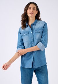Camicia in denim azzurro chiaro con maniche lunghe arrotolate, dotata di due taschini sul petto, chiusura a bottoni e design del colletto classico.