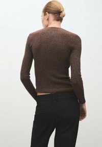 Brązowy sweter prążkowany z długimi rękawami, dopasowany krój i okrągły dekolt, połączony z czarnymi spodniami w kant.