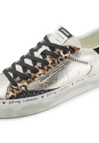 Le sneaker presenta dettagli in oro metallico, stampa leopardata e accenti neri. Lacci neri piatti, suola in gomma testurizzata con marchio sul lato.