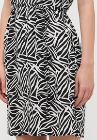 Haljina u crno-bijeloj boji s uzorkom zebra pruga, s gumbima na prednjoj strani, detaljem uvučenog struka i laganom teksturom tkanine.