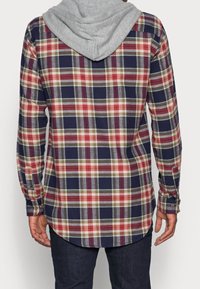 Károvaná košile s šedou mikinou. Obsahuje náměstní, červenou a zelenou kostkovanou strukturu, dlouhé rukávy a zaoblený lem. Zapínací manžety a detaily na límci.