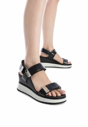 Sandalias de cuña negras con correas de cuero, cierres ajustables en el tobillo y en los dedos, y una suela de goma blanca sutil.
