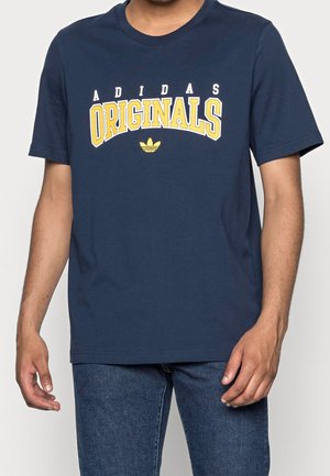 T-shirt en coton bleu marine affichant « ADIDAS ORIGINALS » en texte jaune avec le logo Adidas au-dessus, manches courtes et coupe classique.