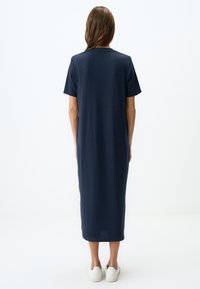 Abito midi blu navy in tessuto a costine, maniche corte, taglio dritto, scende sotto al ginocchio, abbinato a scarpe bianche.
