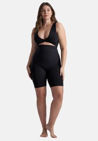 Bañador negro de una pieza con escote pronunciado, detalles recortados en la cintura y un diseño ajustado con una parte inferior estilo pantalón corto.