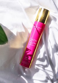 Satin Glow sololja i en ljusrosa flaska med gulddetaljer. Innehåller SPF 15, icke-fet fin spray, vitaminer och arganolja.