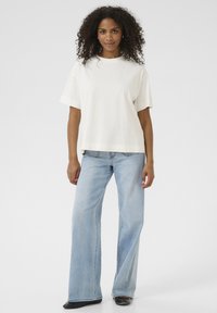T-shirt en coton blanc à manches courtes et coupe ample, associée à un jean large bleu clair et des chaussures noires. Design minimaliste.