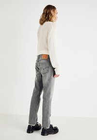 Grå denim jeans med avslappet passform, med et lærpatch bak og en teksturert, strikket hvit genser. Svarte platåsko.