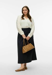 Blouse blanche texturée à manches souples, jupe longue marine, sac à main en cuir marron, et chaussures plates assorties marron.