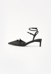 Talons hauts slingback en cuir noir avec un orteil pointu, de fines lanières autour de la cheville, des accents en métal doré et un talon fin. Texture lisse et design minimal.
