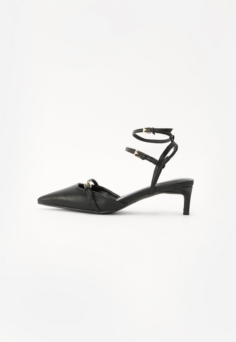 Zapatos de tacón negro de cuero con tiras traseras, puntera afilada, correas delgadas en el tobillo, detalles en hardware dorado y un tacón delgado. Textura suave y diseño minimalista.